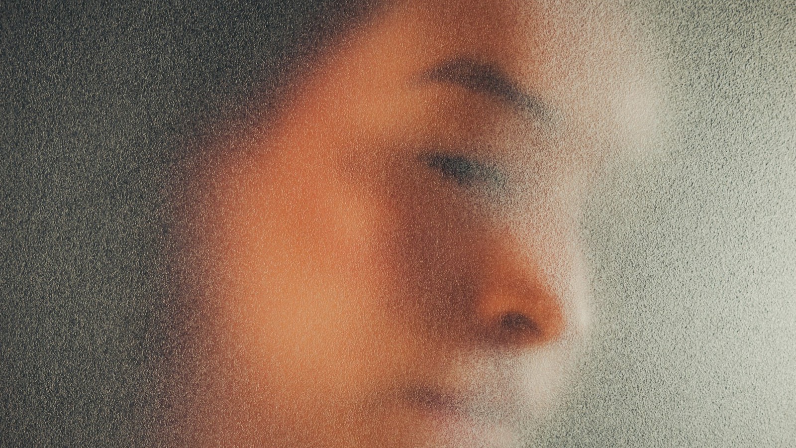 A person's face blurred beyond recognition behind frosted glass